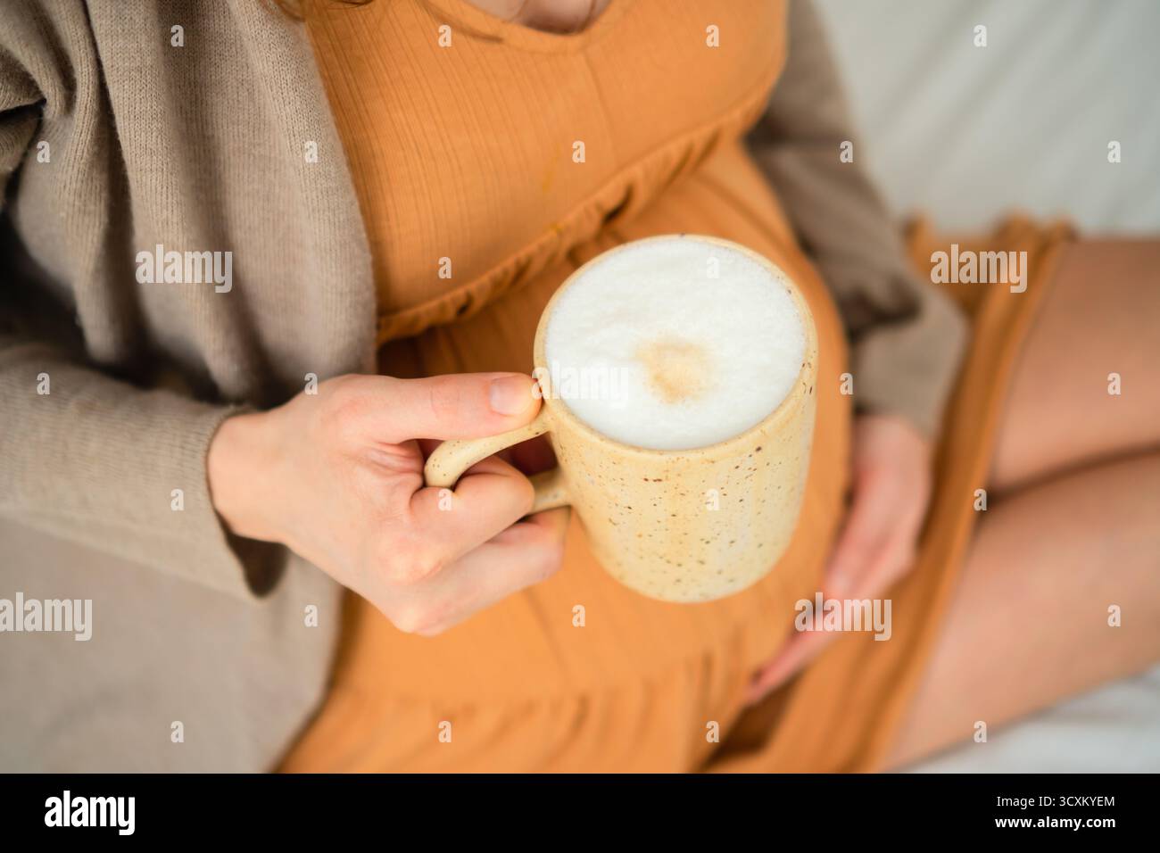 La futura mamma sorseggia una bevanda calda a base di caffè in un ambiente tranquillo. Discussione sull'assunzione responsabile di caffeina durante il periodo di gestazione. Foto Stock