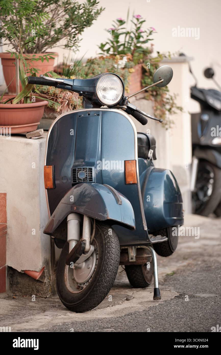 Scooter blu d'epoca parcheggiato in strada vicino a vasi di fiori, simbolo dello stile di vita e del viaggio italiano. Foto Stock