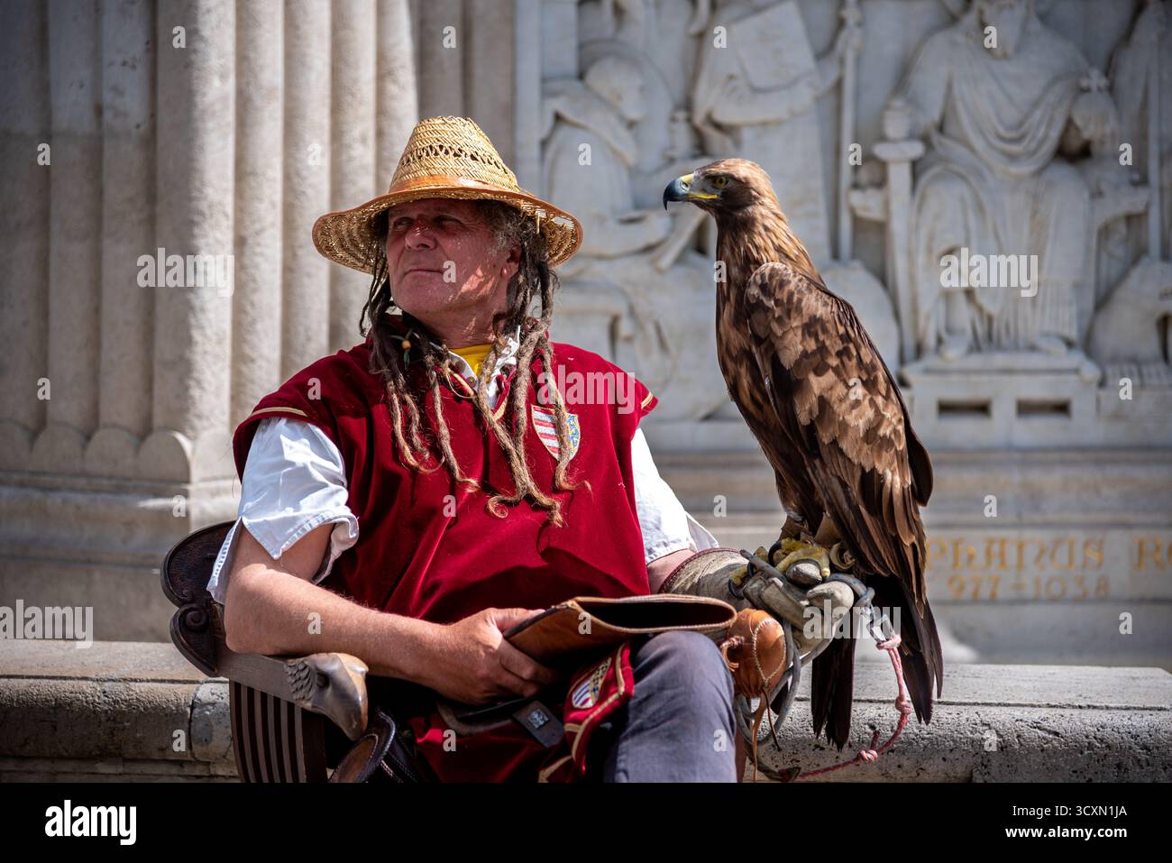 Un falconiere in un cappello di paglia e gilet rosso seduto con un'aquila d'oro sul braccio, a Budapest, in Ungheria, il 30 aprile 2023 Foto Stock