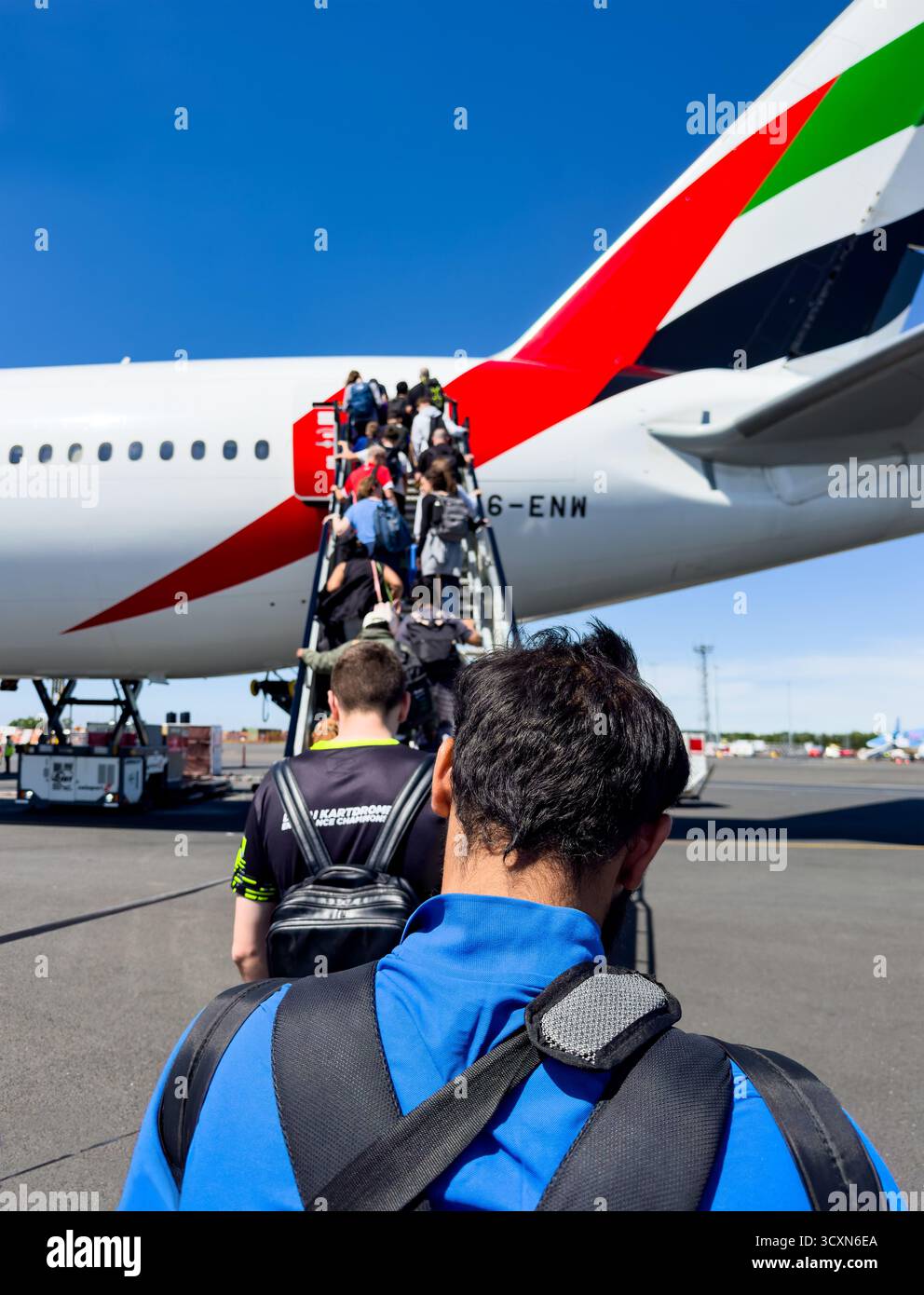 I passeggeri salgono sulle scale della porta posteriore di un aereo Emirates sull'asfalto al Changi Singapore Blue Sky con vivaci colori della coda sullo sfondo Foto Stock
