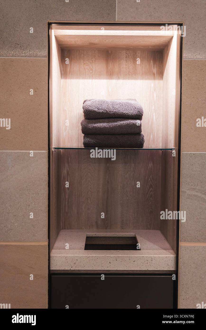 Nicchia in pietra retroilluminata con asciugamani scuri e ripiano in vetro nell'alcova spa Foto Stock