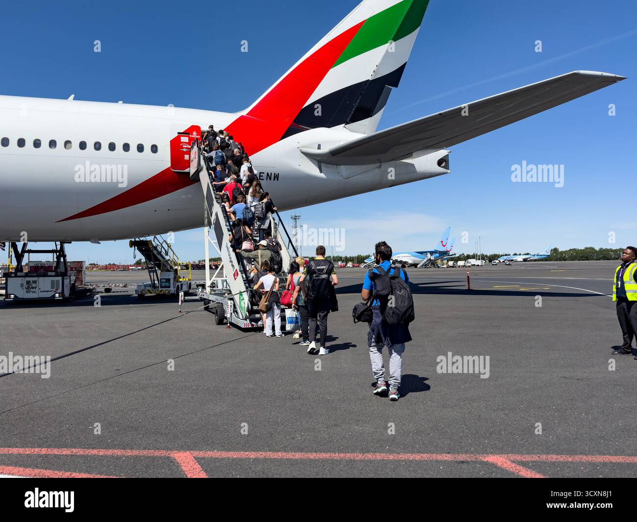 I passeggeri salgono sulle scale della porta posteriore di un aereo Emirates sull'asfalto al Changi Singapore Blue Sky con vivaci colori della coda sullo sfondo Foto Stock