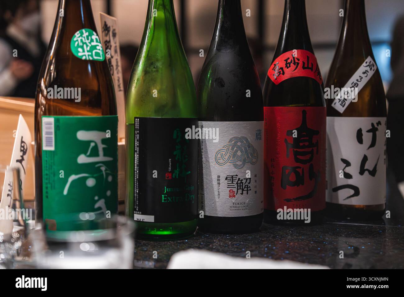 Bottiglie di sake giapponesi sul lucido bancone del bar nella sala di degustazione dell'hotel Foto Stock