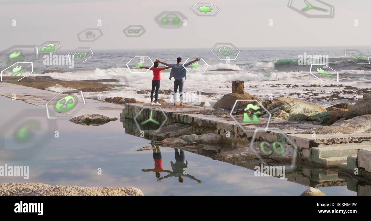 Coppia in piedi con giacca in denim, parte superiore rossa che tiene le mani, braccia allungate sul molo con icone ecologiche Foto Stock