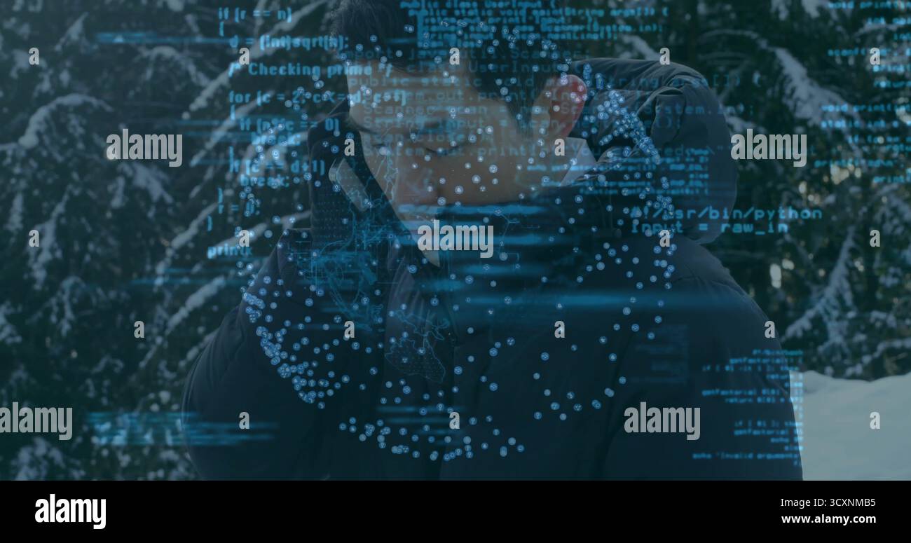 Uomo asiatico parlante che indossa una giacca invernale su smartphone in boschi innevati, sovrapposizione di codice Foto Stock