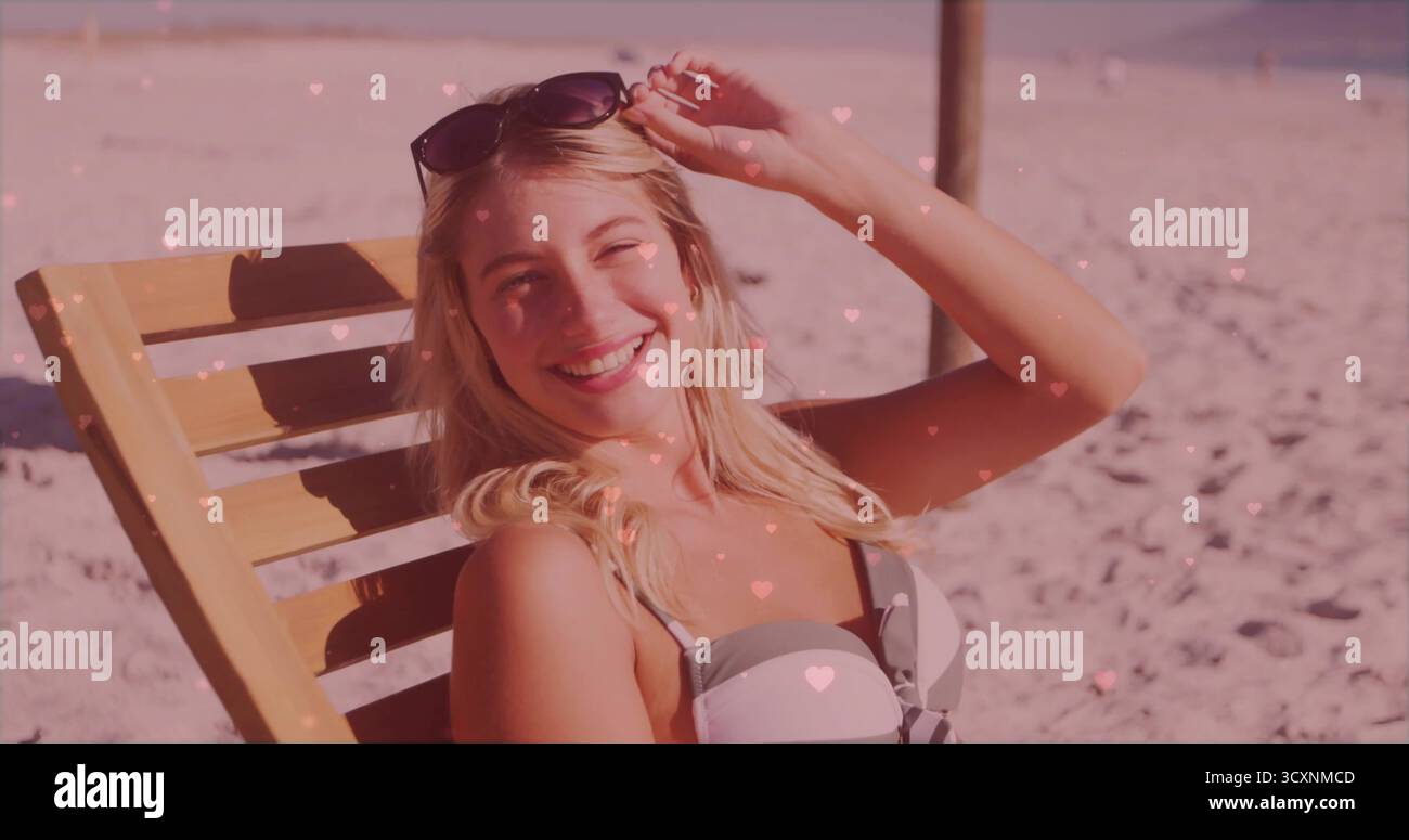 Donna che indossa un paio di occhiali da sole regolabili sulla sedia da spiaggia in riva al mare con cuori rosa, spazio fotocopie Foto Stock