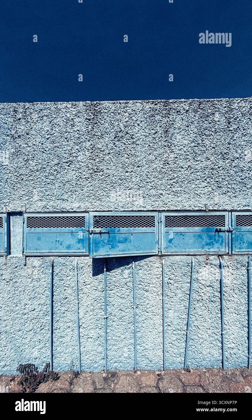 Parete in cemento armato con porte in metallo blu e cielo blu, creando una scena industriale urbana Foto Stock