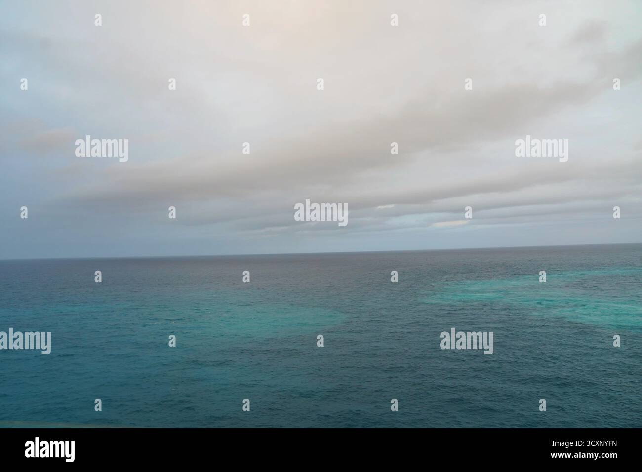 Le calme acque turchesi del Mar dei Caraibi si estendono sotto le morbide nuvole grigie, creando un tranquillo paesaggio marino di tonalità mutevoli e luce sottile Foto Stock