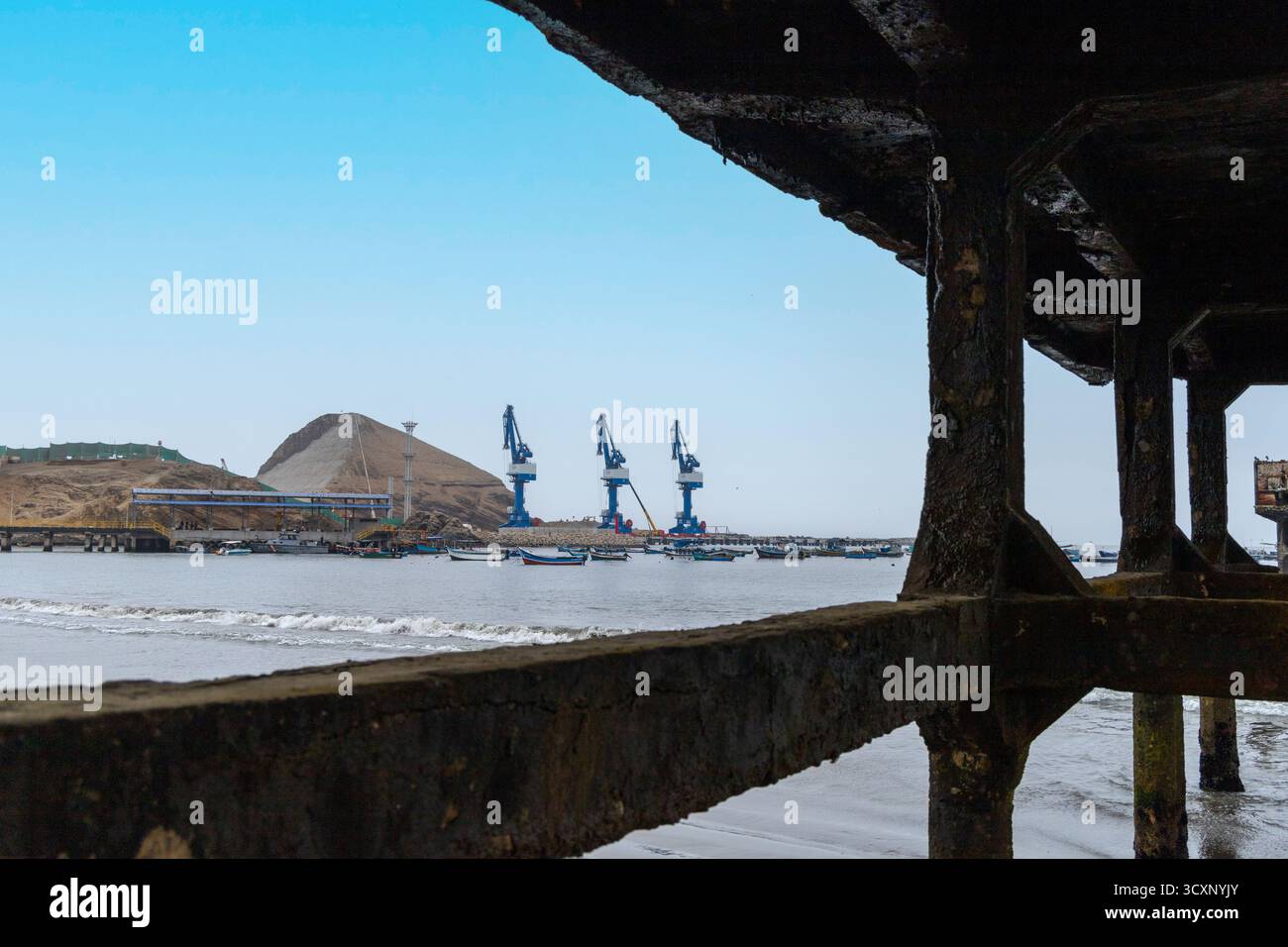 Mega port Chancay. Un molo con vista su un grande specchio d'acqua e una collina sullo sfondo. Il molo è pieno di barche e gru Foto Stock Mega port Chancay. Un molo con vista su un grande specchio d'acqua e una collina sullo sfondo. Il molo è pieno di barche e gru Foto Stock