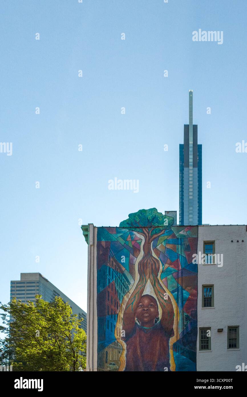 Un murale di un uomo che tiene un albero su un edificio. Il murale è colorato e ha un senso di speranza e crescita Foto Stock Un murale di un uomo che tiene un albero su un edificio. Il murale è colorato e ha un senso di speranza e crescita Foto Stock
