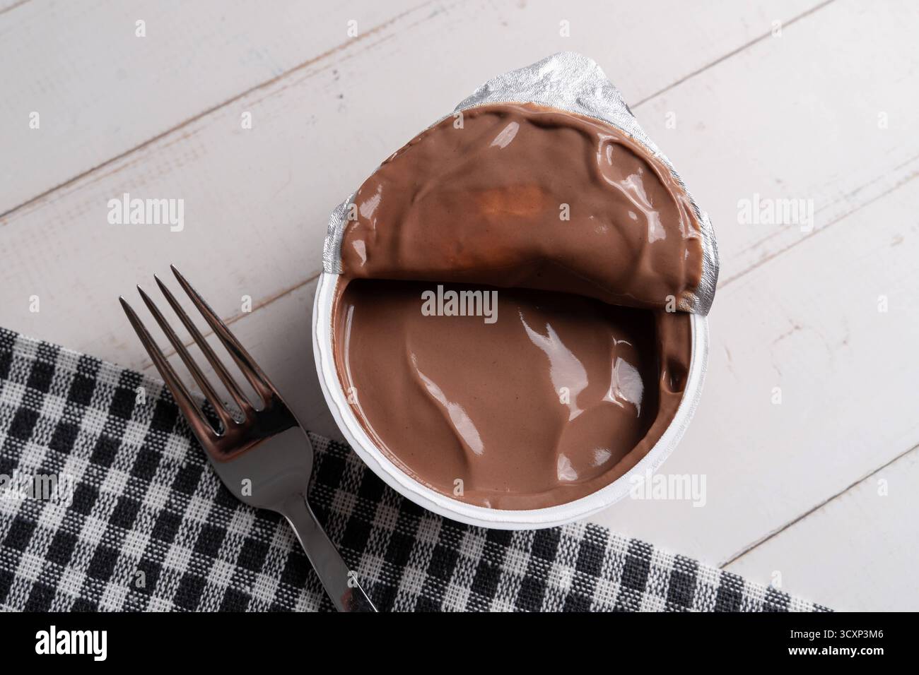 Baviera, Germania - 15 ottobre 2025: La tendenza a mangiare pudding con una forchetta si sta diffondendo rapidamente sui social media e sta scatenando un dibattito. Accanto a una forchetta si trova una tazza aperta di budino al cioccolato che simboleggia una bizzarra tendenza alimentare. *** Der Trend, Pudding mit einer Gabel zu essen, verbreitet sich rasant in sozialen Medien und sorgt für Diskussionen. Ein offener Schokopuddingbecher liegt neben einer Gabel Sinnbild eines skurrilen Foodtrends. Foto Stock