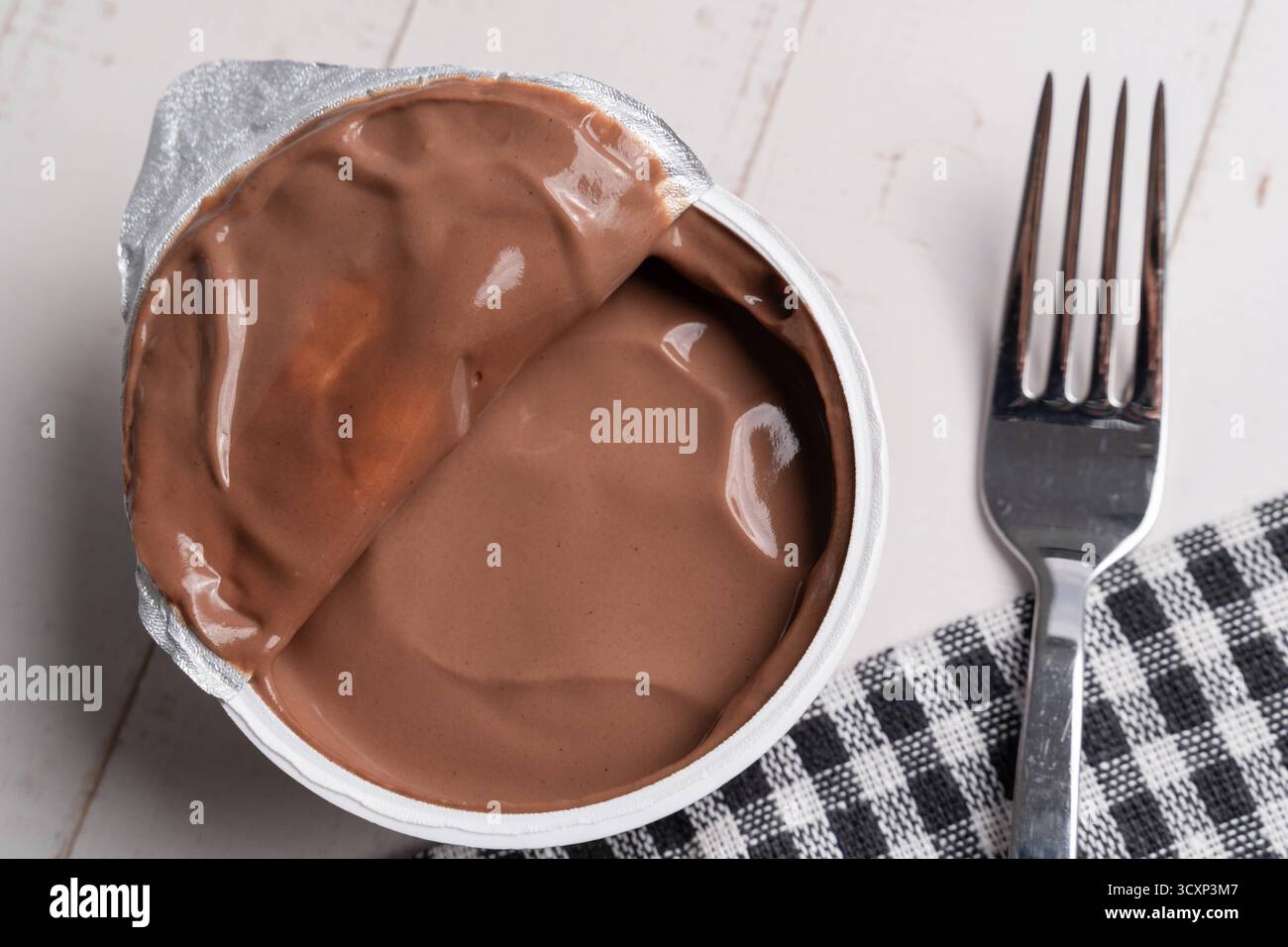 Baviera, Germania - 15 ottobre 2025: La tendenza a mangiare pudding con una forchetta si sta diffondendo rapidamente sui social media e sta scatenando un dibattito. Accanto a una forchetta si trova una tazza aperta di budino al cioccolato che simboleggia una bizzarra tendenza alimentare. *** Der Trend, Pudding mit einer Gabel zu essen, verbreitet sich rasant in sozialen Medien und sorgt für Diskussionen. Ein offener Schokopuddingbecher liegt neben einer Gabel Sinnbild eines skurrilen Foodtrends. Foto Stock