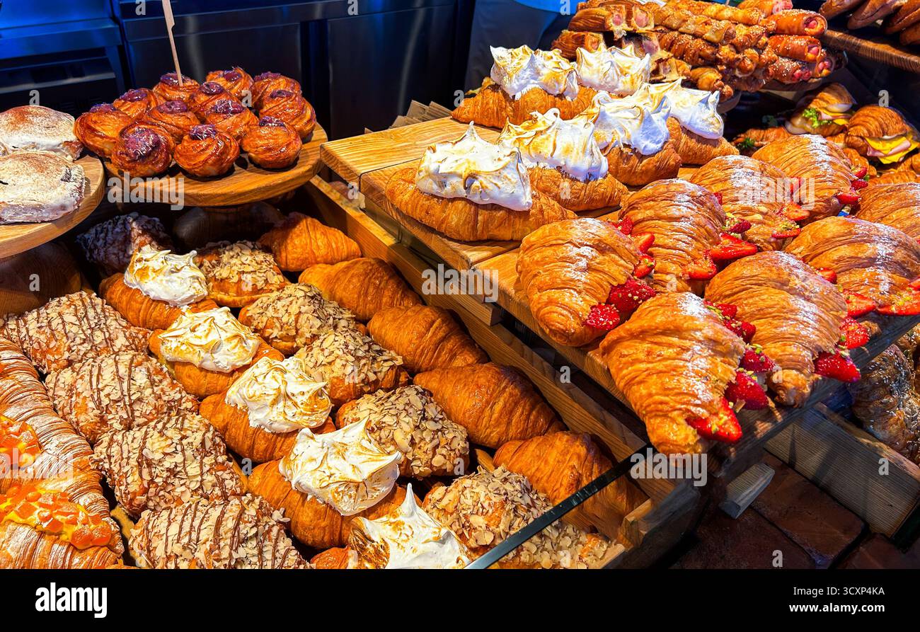 Croissant e dolci di pasticceria dorati con condimenti esposti sulla vetrina del negozio di panetteria. Cibo delizioso da asporto. Foto Stock