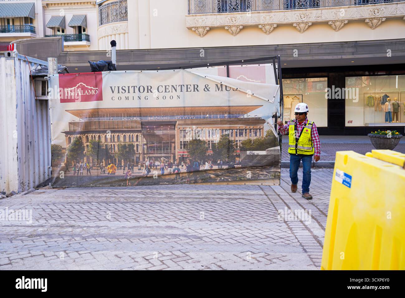 Un operaio edile passa davanti a uno striscione che mostra i progetti per il Centro visitatori e Museo Alamo, parte di una riqualificazione in corso a San Antonio Foto Stock