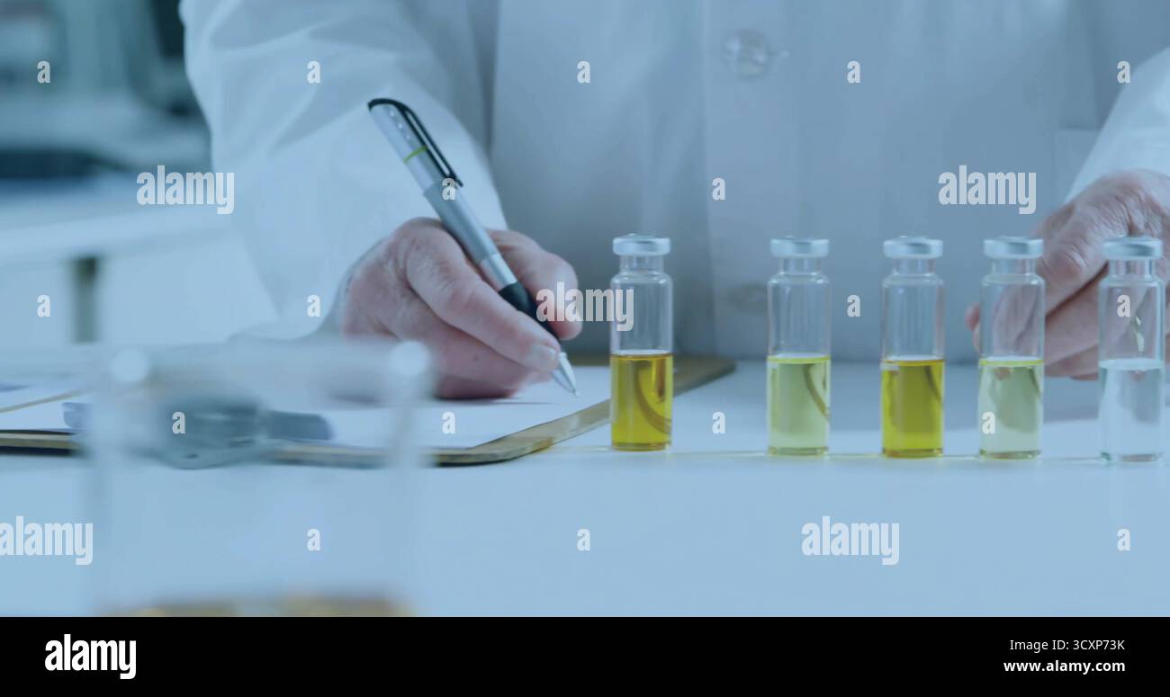 Scrivendo scienziato di laboratorio che esamina fiale gialle al banco clinico, penna e appunti in mano Foto Stock