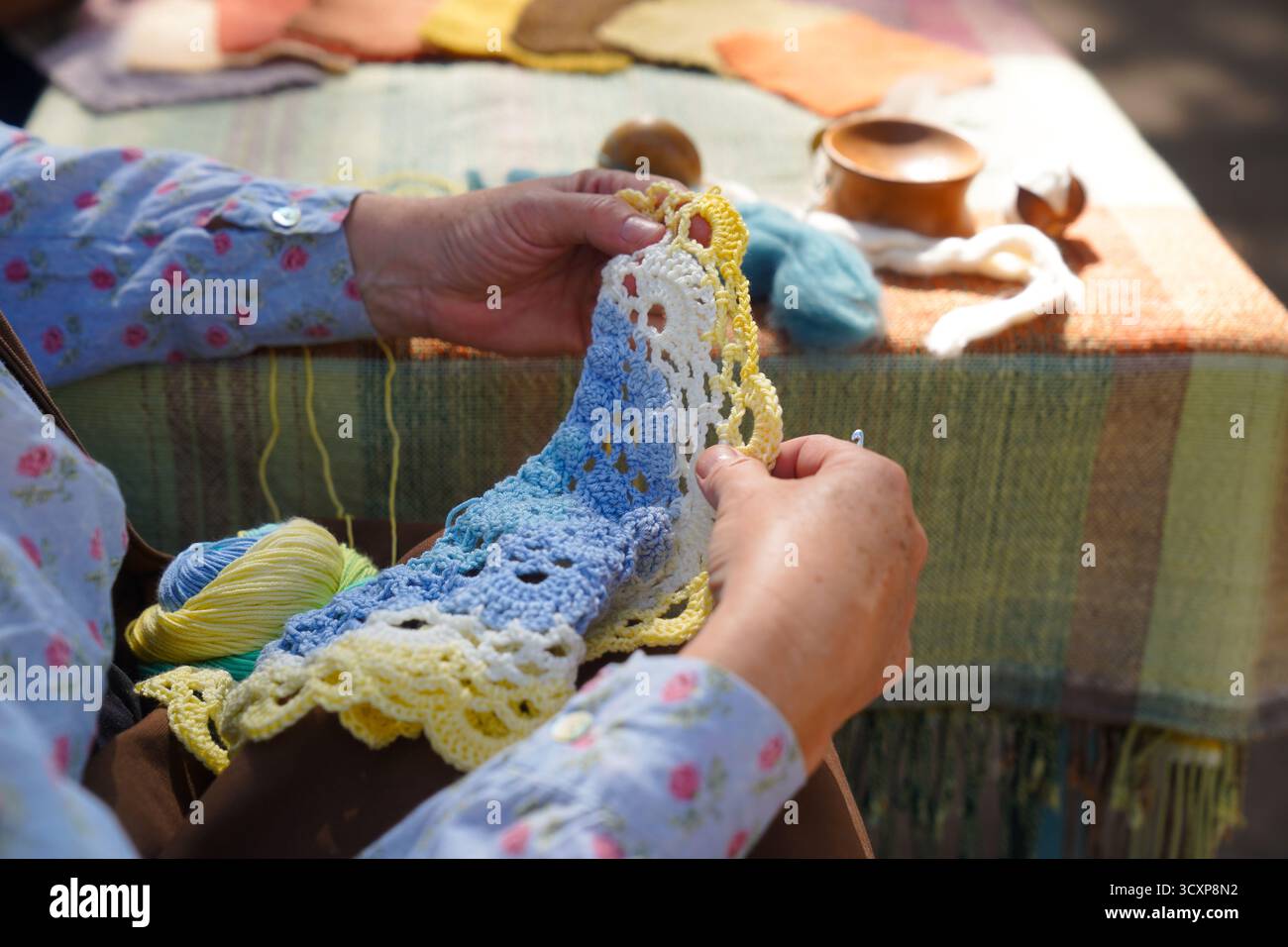 Mani che uniscono filati colorati su una superficie tessile intrecciata. Una vista macro dettagliata che mette in risalto l'arte e la consistenza dell'artigianato artigianale Foto Stock
