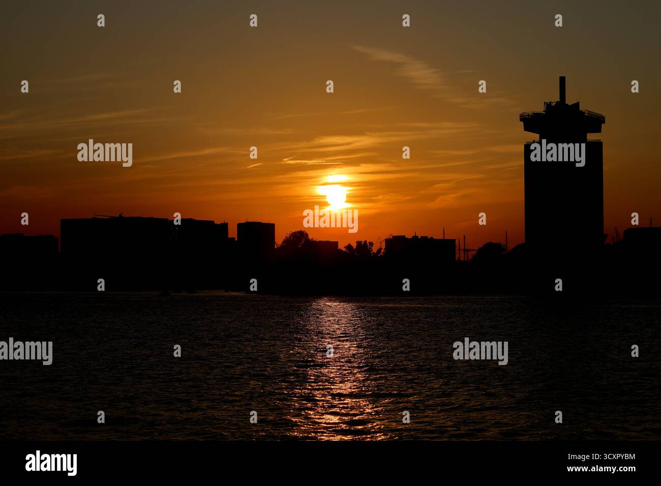 Tramonto sul fiume IJ con il profilo della torre A'DAM Lookout e i blocchi della città all'orizzonte sotto le nuvole striate ad Amsterdam, Paesi Bassi. Foto Stock