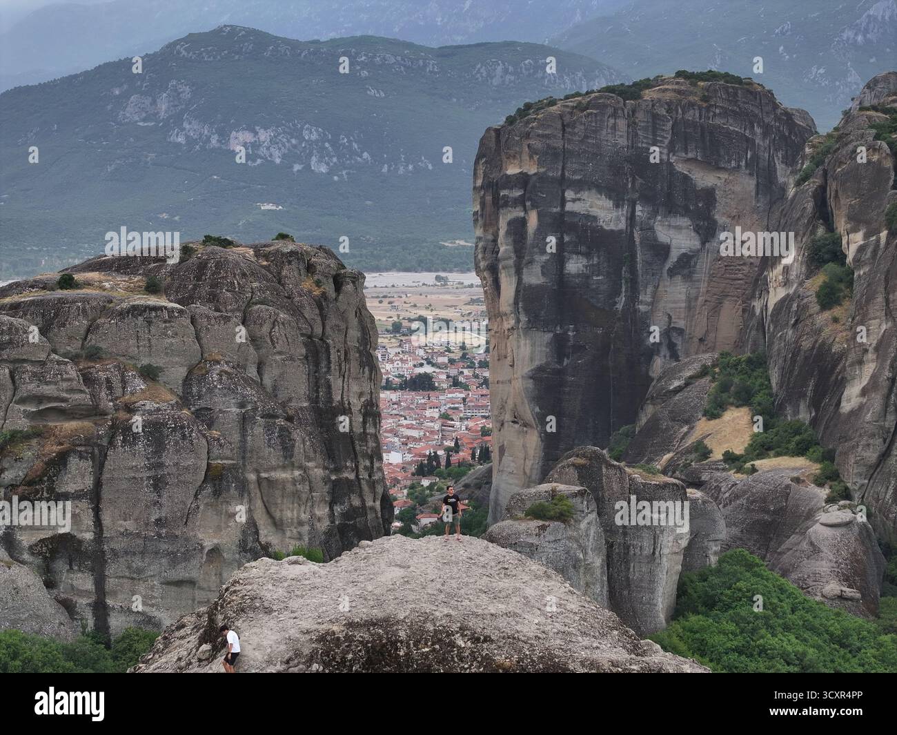 Persone che esplorano i torreggianti pilastri di roccia di meteora che si affacciano sulla tradizionale città di kalabaka nella valle sottostante, mostrando scogliere spettacolari e monaste Foto Stock