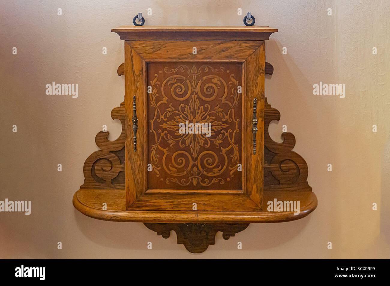 Un armadio in legno decorato con pareti beige, con intricate incisioni e un design ad arco, caratterizzato da un pannello decorativo centrale che ne esalta la Foto Stock