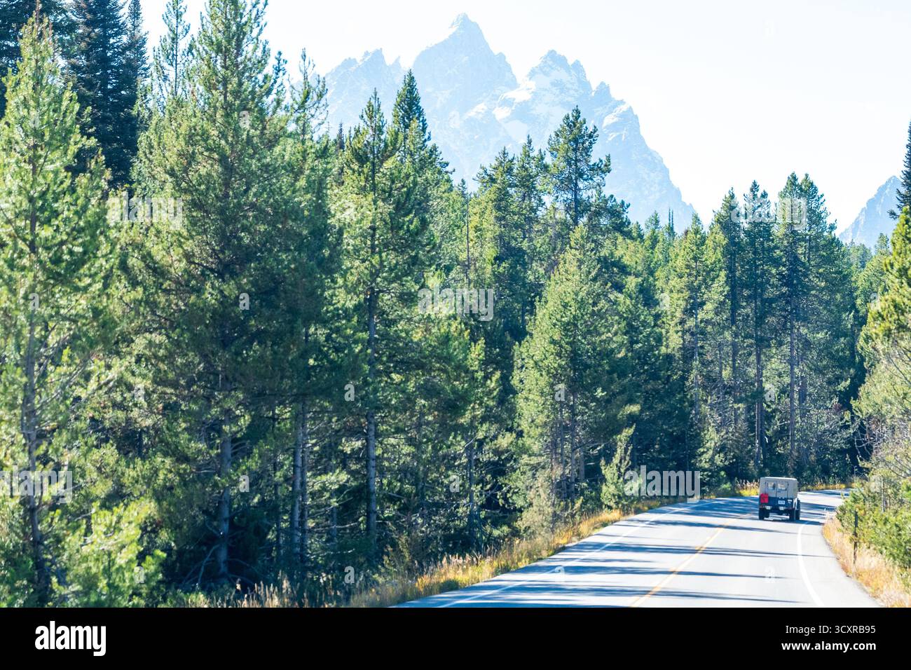 Teton Road è fiancheggiata da fitte foreste di conifere che conducono verso le maestose Teton Mountains. Un solo veicolo viaggia da solo sulla strada Foto Stock