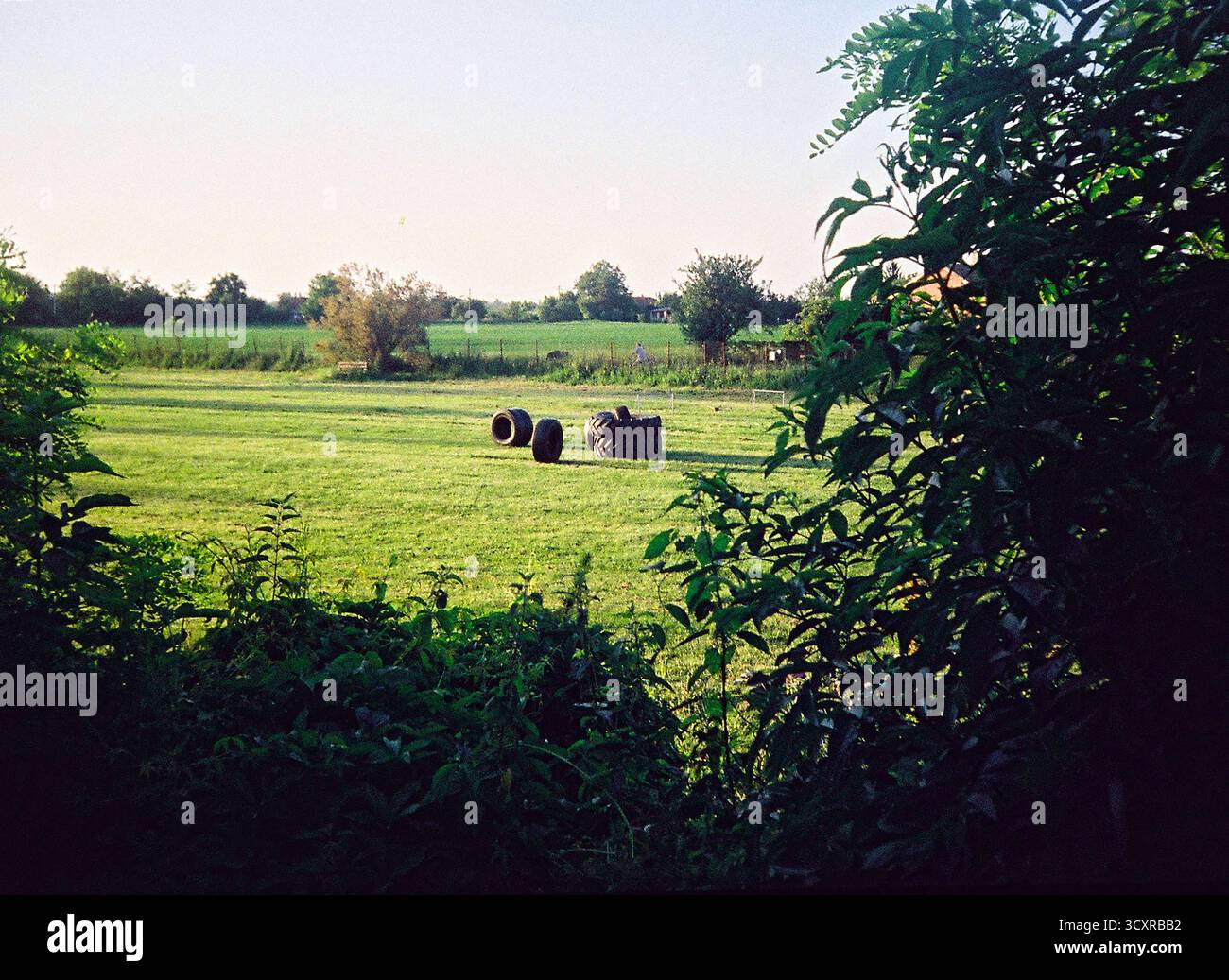 GROSSI pneumatici per trattore usati per l'allenamento di forza su un campo da calcio locale, fotografati sotto il sole splendente con un'estetica autentica del film analogico. Foto Stock