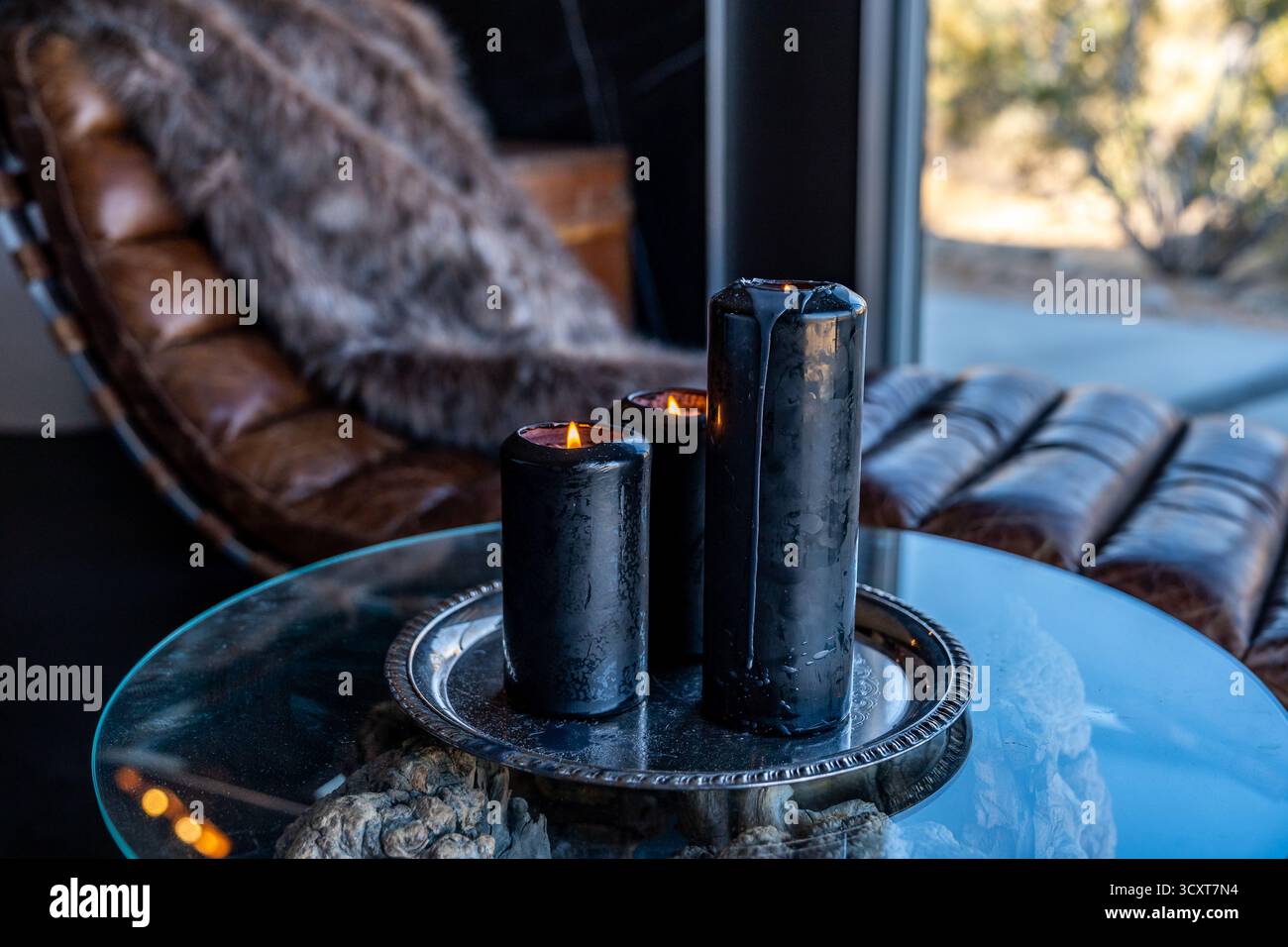 Candele nere che bruciano fiamma su un piatto di peltro d'argento su un tavolo di vetro accanto alla poltrona in pelle Foto Stock