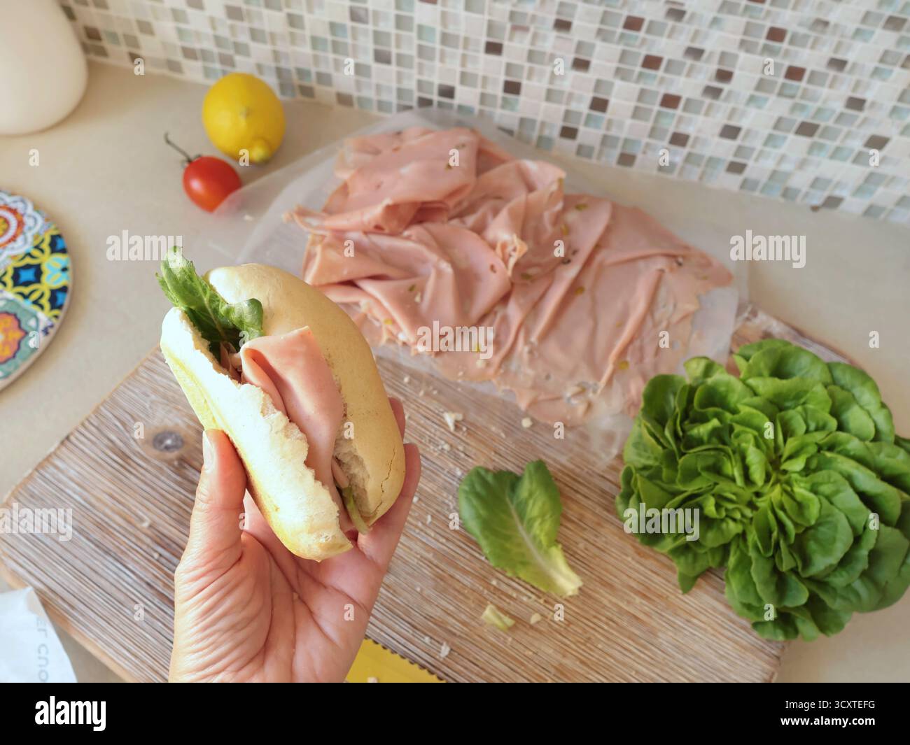 Una persona anonima prepara un panino con salsiccia, lattuga e mortadella, maionese fatta in casa in cucina. Cucina italiana, alta qualità coltivata in azienda Foto Stock