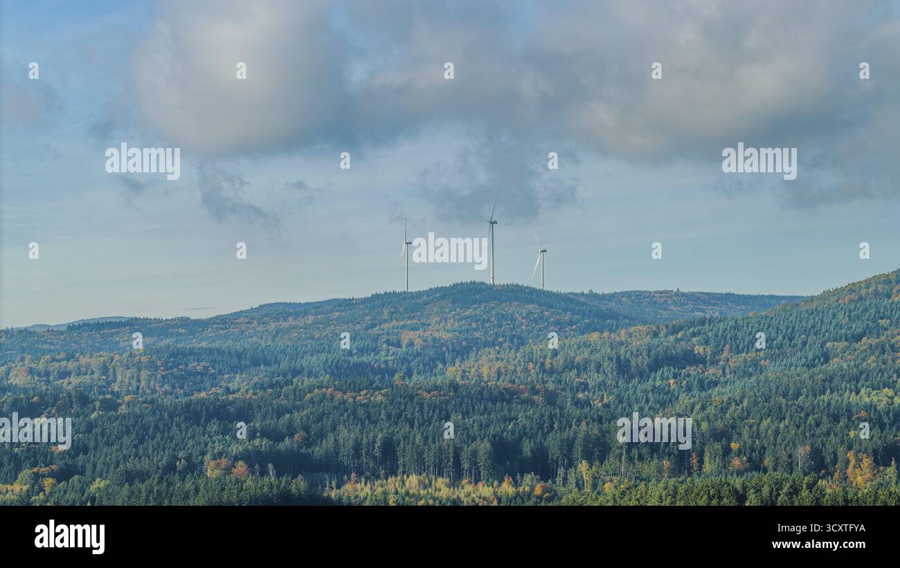 Tre turbine eoliche sorgono su una collina, circondate da fitte foreste. Il cielo è limpido con poche nuvole, creando una tranquilla atmosfera autunnale. Krumbach Foto Stock