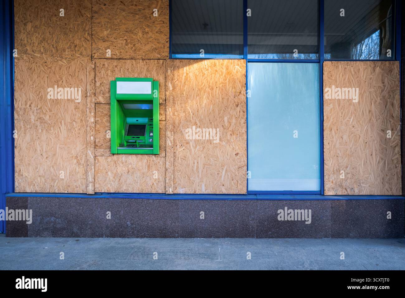 ATM verde in piedi vicino a un fronte di magazzino frantumato con compensato dopo un attacco aereo russo, simboleggiando la resilienza in mezzo alla distruzione: 16 ottobre 2025, Kiev, Ucraina Foto Stock