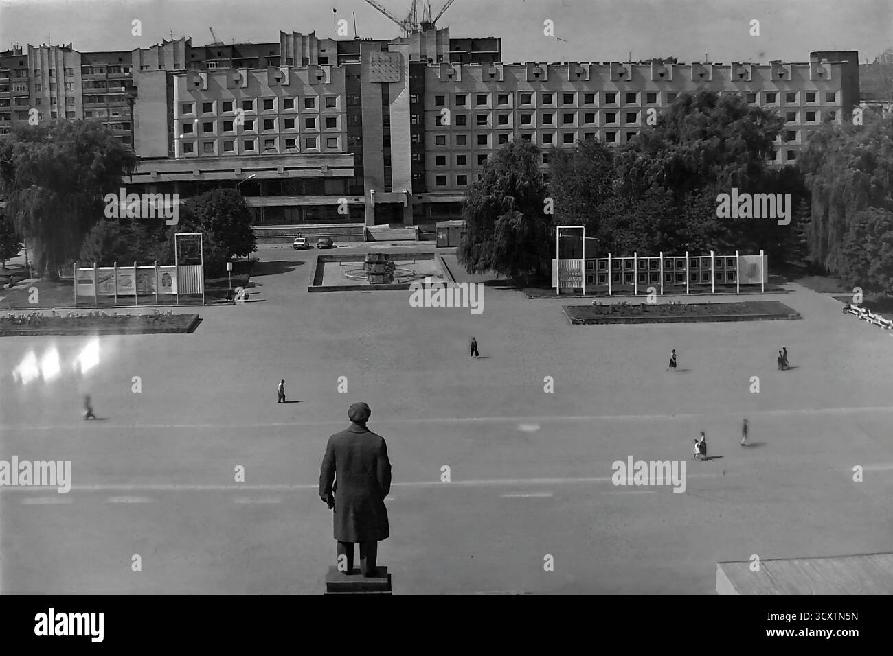 Un'ampia foto d'archivio ad alto angolo degli anni '1980, che si affaccia su Piazza della Rivoluzione d'ottobre (ora Piazza Soborna) da dietro il monumento Lenin a Sloviansk. La vista cattura il vasto spazio pubblico aperto con un imponente edificio di epoca sovietica in costruzione sullo sfondo, sormontato da gru a torre. Questa immagine illustra con forza la portata monumentale della pianificazione urbana sovietica e l'attenzione dell'epoca sullo sviluppo. E' un prezioso resoconto storico della vita cittadina in un tranquillo Donbas prima della guerra Foto Stock
