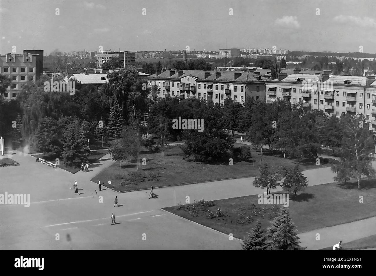 Una foto d'archivio ad alto angolo degli anni '1980 cattura una vista serena di Piazza della Rivoluzione d'ottobre (ora Piazza Soborna) e del suo parco adiacente a Sloviansk. I pedoni passeggiano piacevolmente lungo i sentieri dello spazio verde ben tenuto. Sullo sfondo, una linea di tipici edifici di epoca sovietica si erge sullo skyline più ampio della città. Questa immagine cattura perfettamente il ritmo calmo della vita quotidiana e del tempo libero pubblico in un tranquillo Donbas prima della guerra Foto Stock
