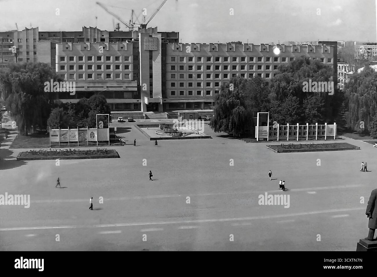 Un'ampia foto d'archivio ad alto angolo degli anni '1980, che si affaccia su Piazza della Rivoluzione d'ottobre (ora Piazza Soborna) da dietro il monumento Lenin a Sloviansk. La vista cattura il vasto spazio pubblico aperto con un imponente edificio di epoca sovietica in costruzione sullo sfondo, sormontato da gru a torre. Questa immagine illustra con forza la portata monumentale della pianificazione urbana sovietica e l'attenzione dell'epoca sullo sviluppo. E' un prezioso resoconto storico della vita cittadina in un tranquillo Donbas prima della guerra Foto Stock