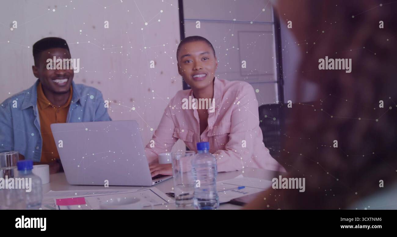 Donna collaboratrice con una camicia rosa con bottoni che utilizza un computer portatile nella sala riunioni dell'ufficio con carte e tazze Foto Stock