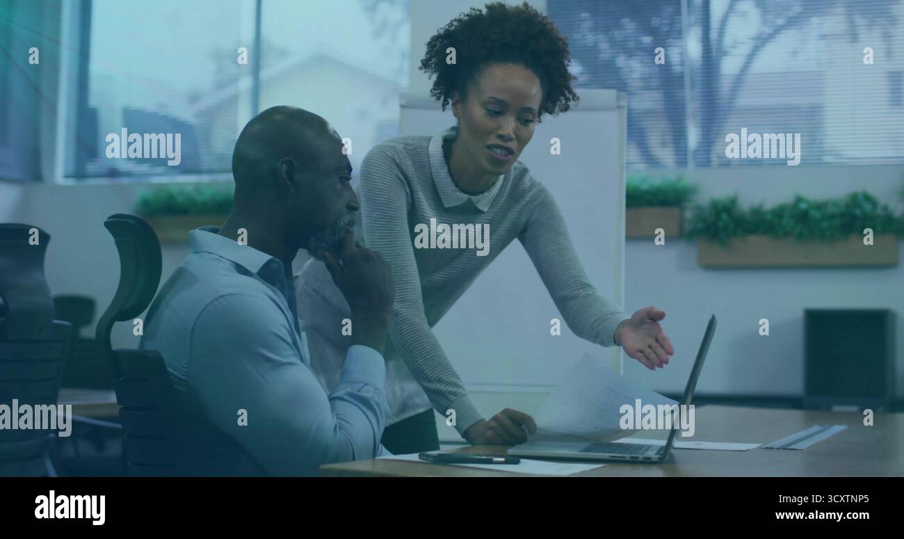 Collaborazione con i colleghi che esaminano documenti stampati presso la scrivania della sala riunioni, con schermo per laptop Foto Stock
