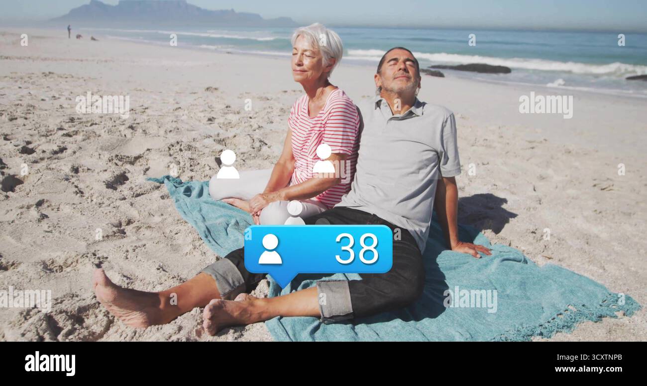 Coppia rilassante che indossa abiti informali appoggiati alle mani sulla spiaggia sabbiosa, con telo da spiaggia blu Foto Stock