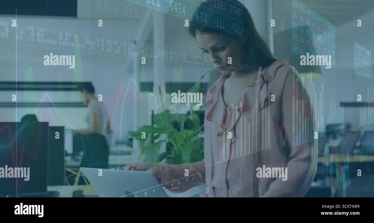 Analisi dei dati di mercato, donna in camicetta rosa che esamina il laptop alla scrivania dell'ufficio, con impianto in vaso Foto Stock