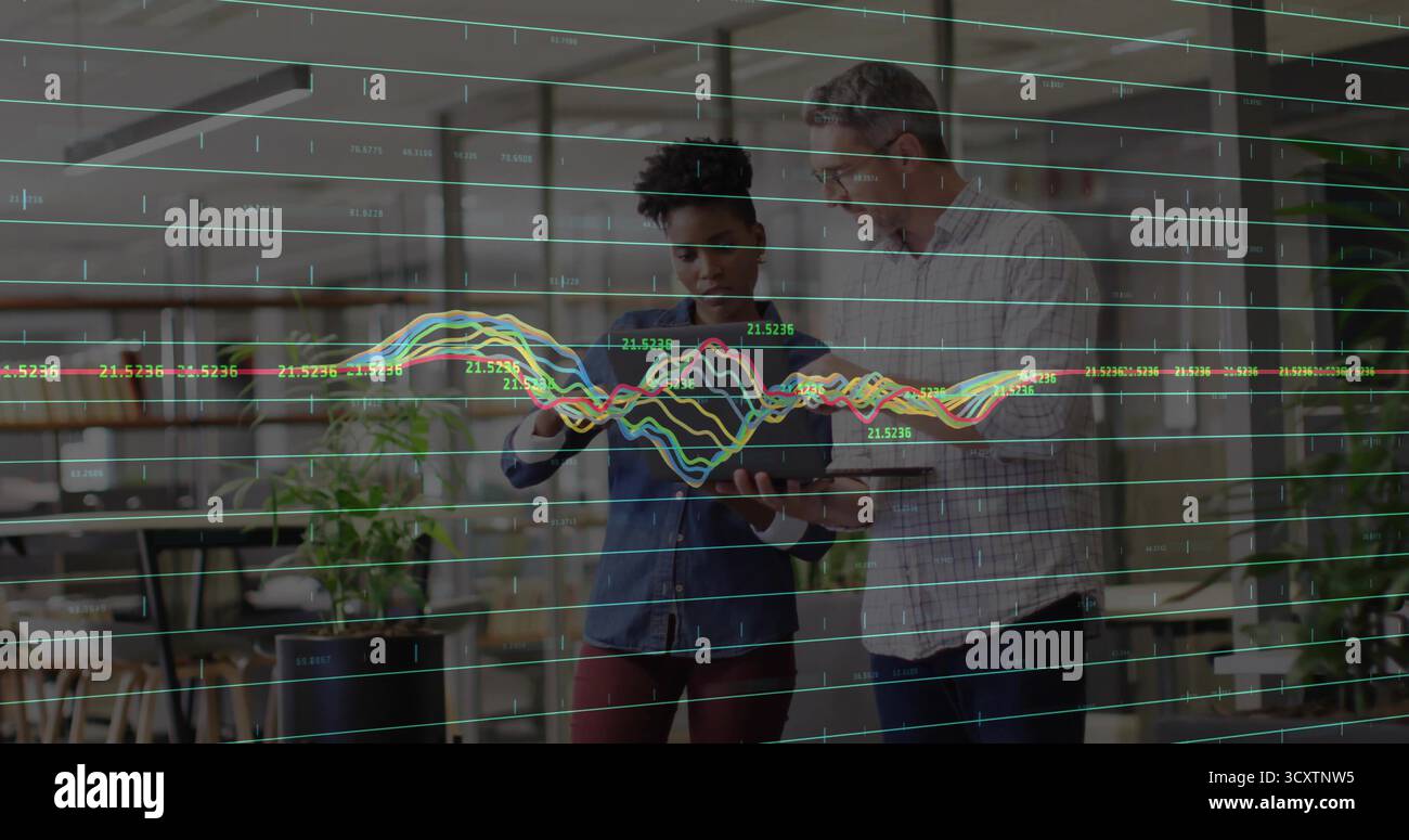 Esame di un uomo e una donna tablet che analizzano i dati all'interno di un ufficio open space, con grafici a linee traslucidi Foto Stock