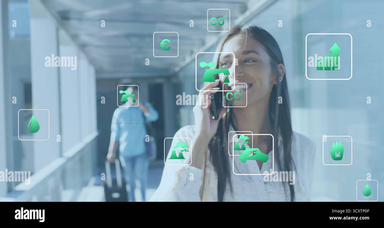 Donna ispanica parlante che usa lo smartphone in un connettore di vetro, con valigia rotolante e icone ecologiche Foto Stock