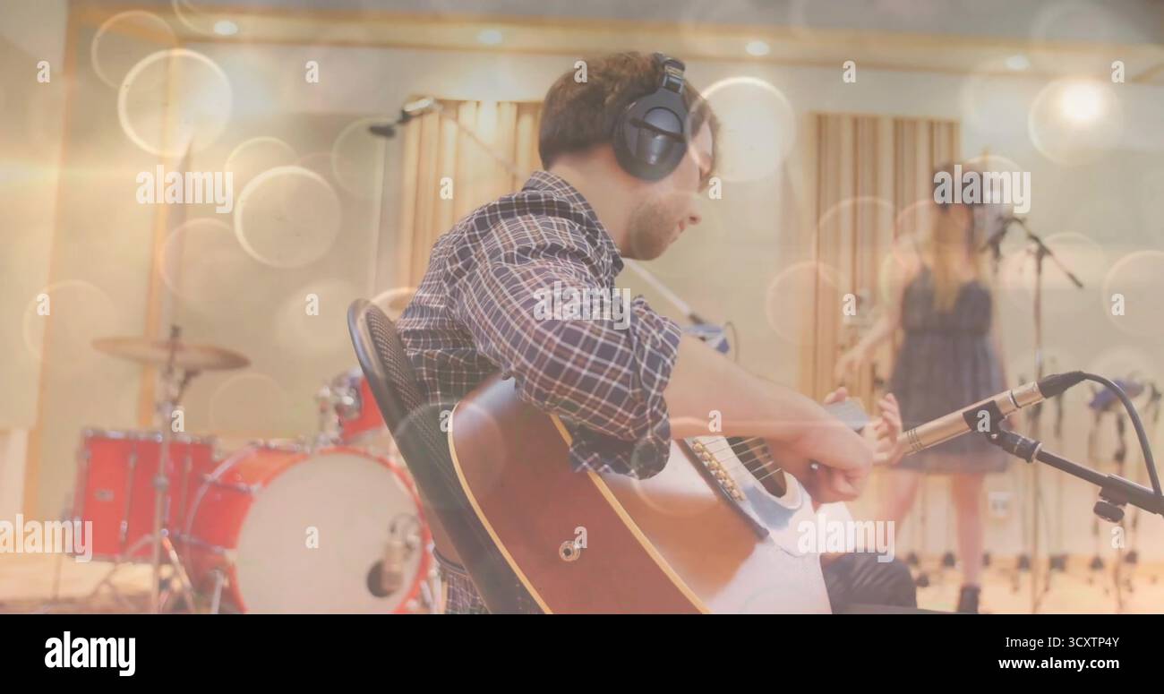Chitarrista maschile che indossa una camicia a quadri, suona la chitarra acustica in studio di registrazione, con batteria rossa Foto Stock