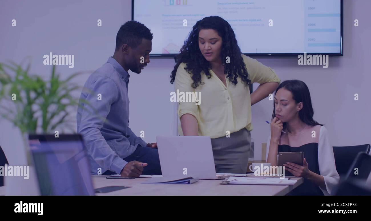 Revisione del team che indica il laptop nella sala conferenze con un collega che tiene in mano un tablet e una penna Foto Stock