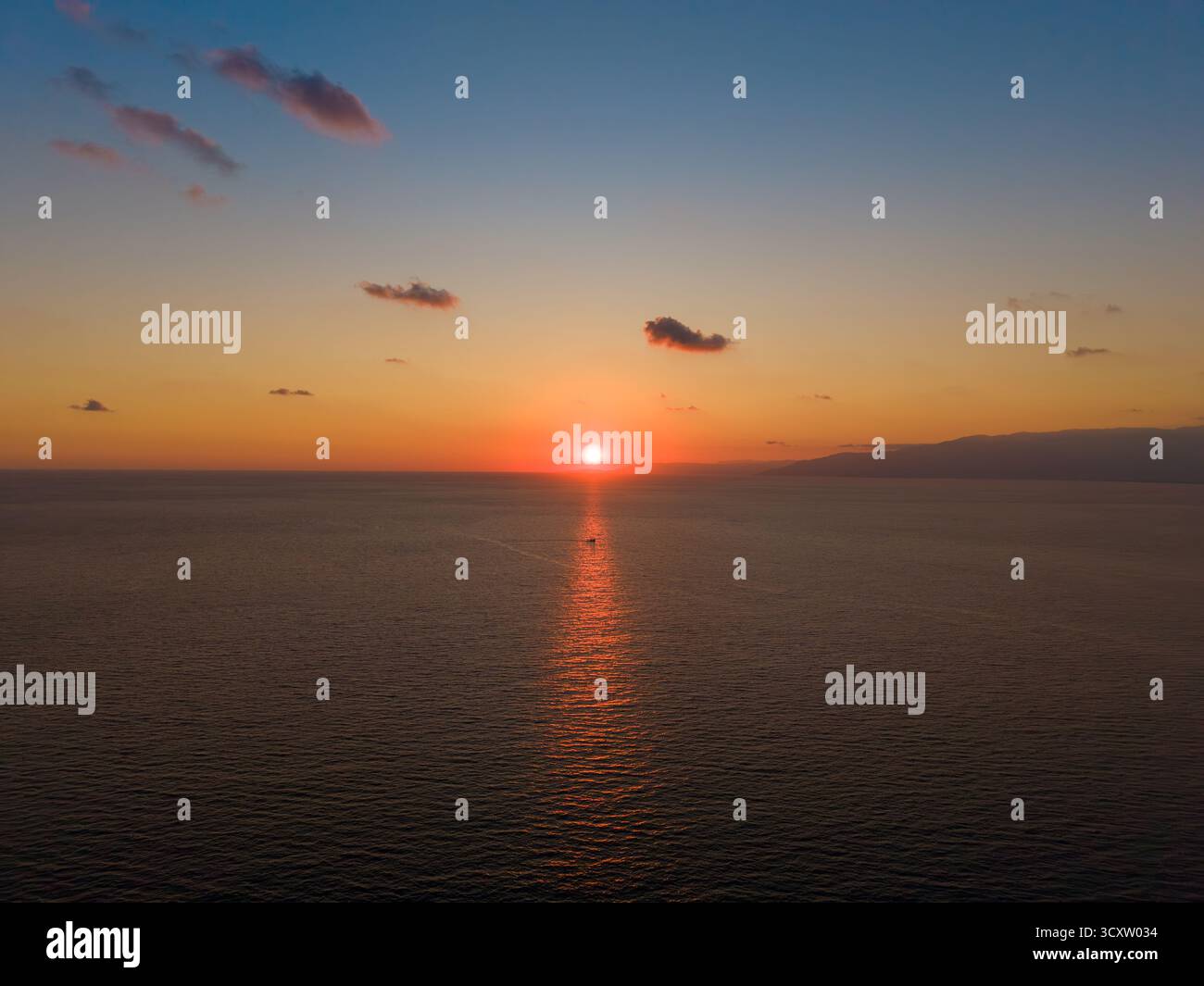 Tramonto dorato che si riflette sul mare con una piccola barca riflessa Foto Stock