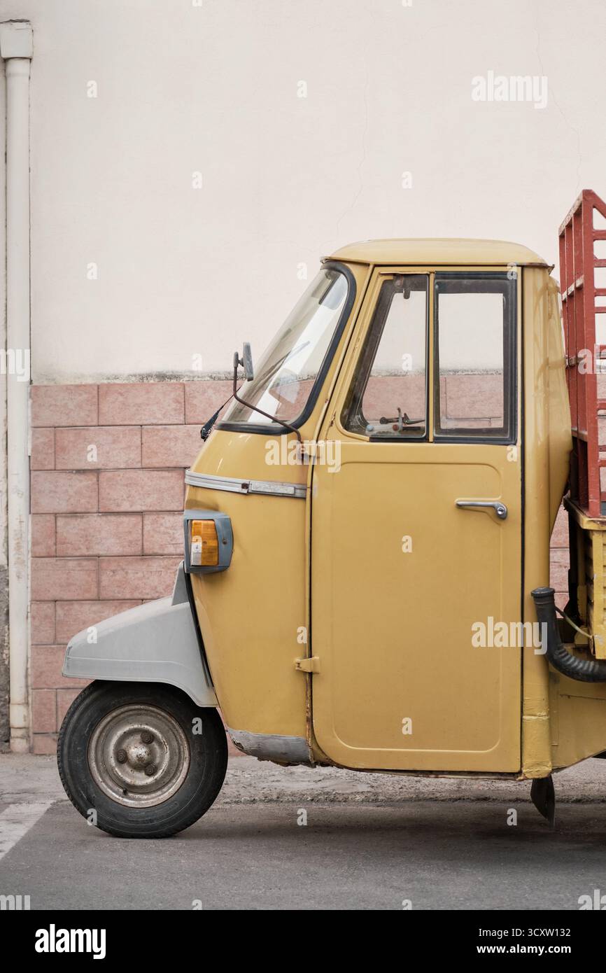Veicolo a tre ruote giallo d'epoca parcheggiato da una parete color pastello in Italia, in stile retrò minimalista. Foto Stock
