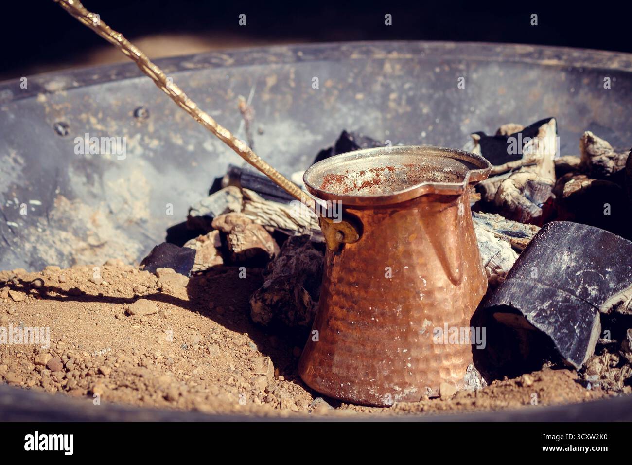 Una tradizionale cezva in rame con manico lungo per preparare caffè arabo forte su brace calde in un vassoio di metallo Foto Stock