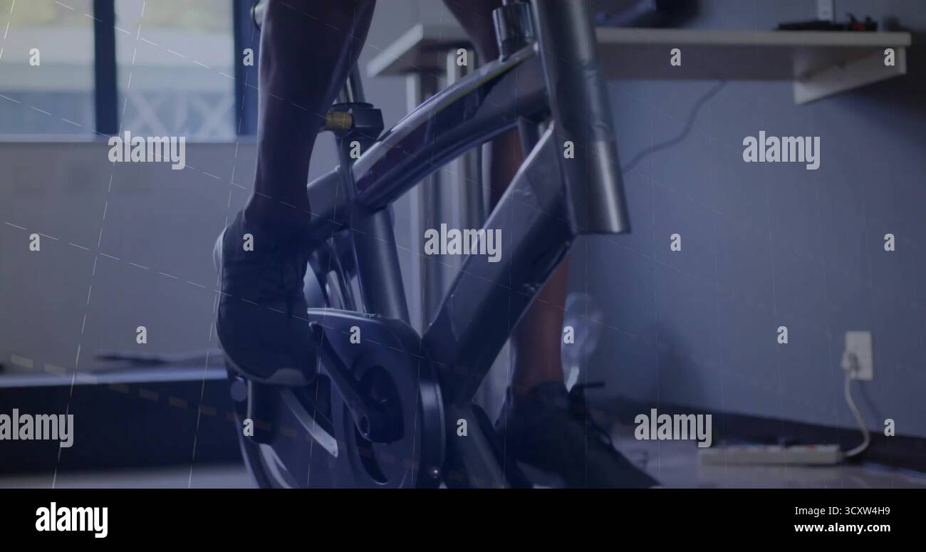 Pedalando maschile indossando pantaloncini neri, sneakers in cyclette in palestra, con cavi da scrivania Foto Stock