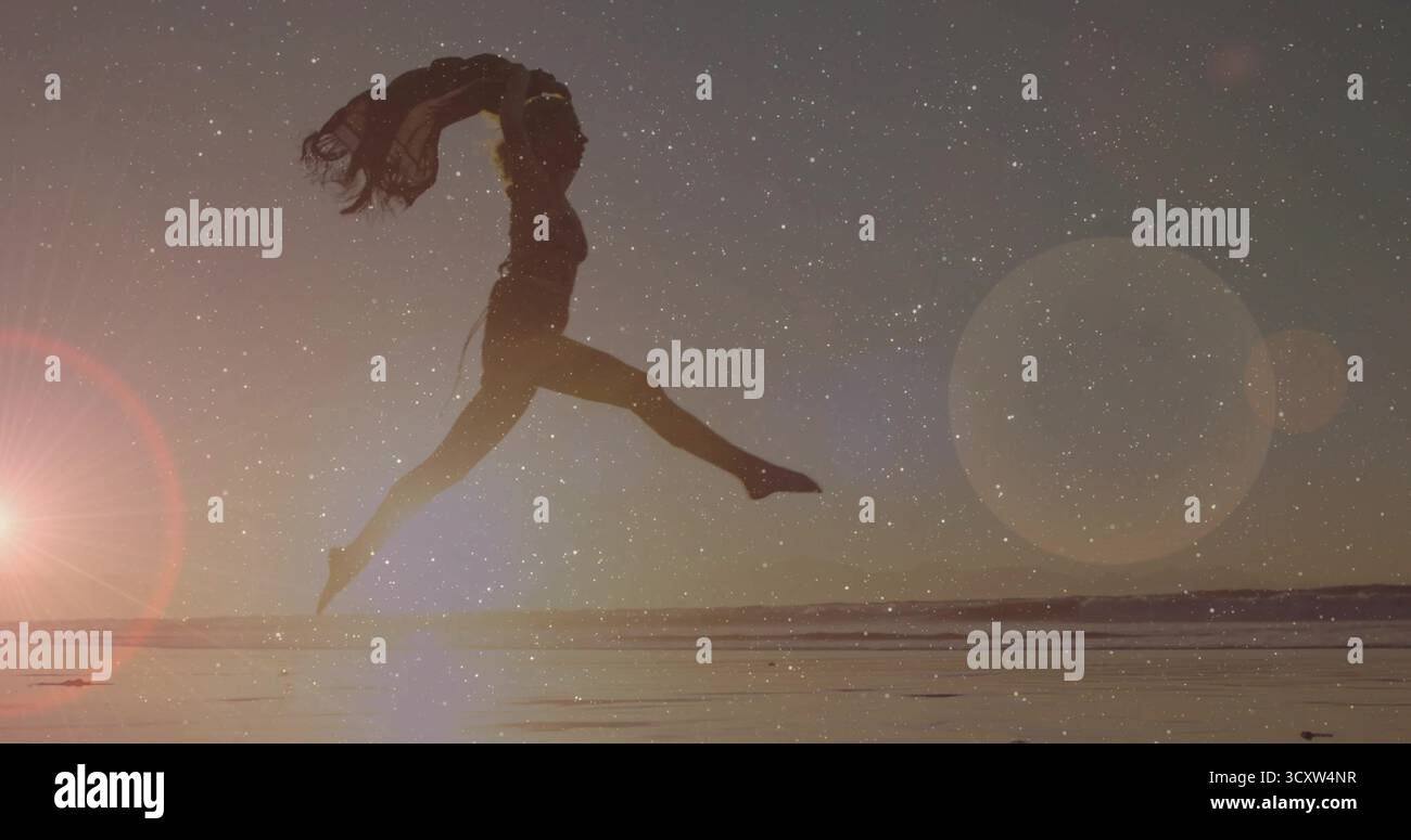 Ballerina di silhouette in un abito fluente che danzava in acqua al tramonto, con tessuto e lucentezza Foto Stock