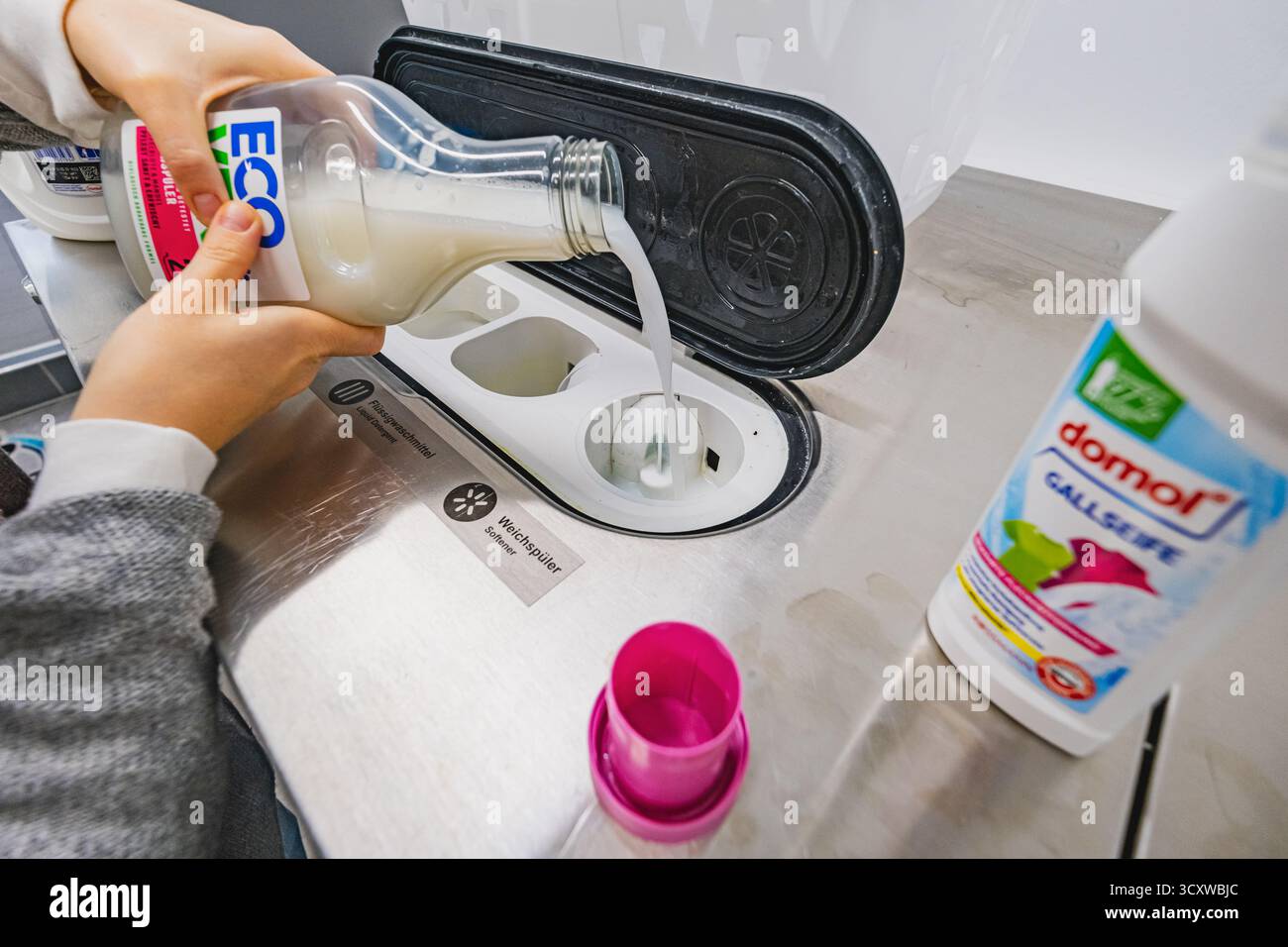 Il cliente riempie la lavatrice con liquido balsamo nella lavanderia self-service Foto Stock