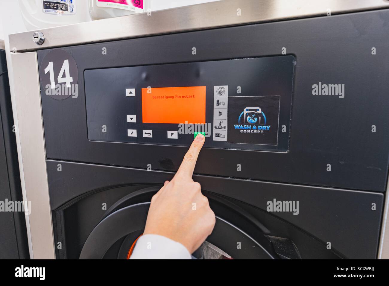 Il cliente preme il pulsante per avviare la lavatrice al servizio di lavanderia self-service Foto Stock
