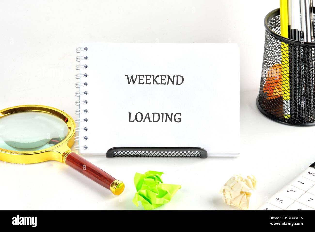 Una scrivania mostra un blocco note con le parole "carico weekend", accompagnato da una lente d'ingrandimento e da una carta colorata. Supporto per penne Foto Stock