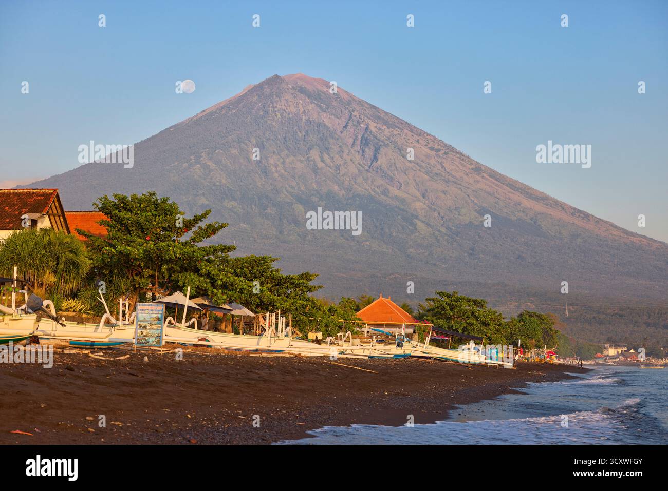 Vista panoramica del vulcano del Monte Agung dalla spiaggia di Amed con la luna piena nel cielo. Amed, Karangasem Regency, Bali, Indonesia. Foto Stock