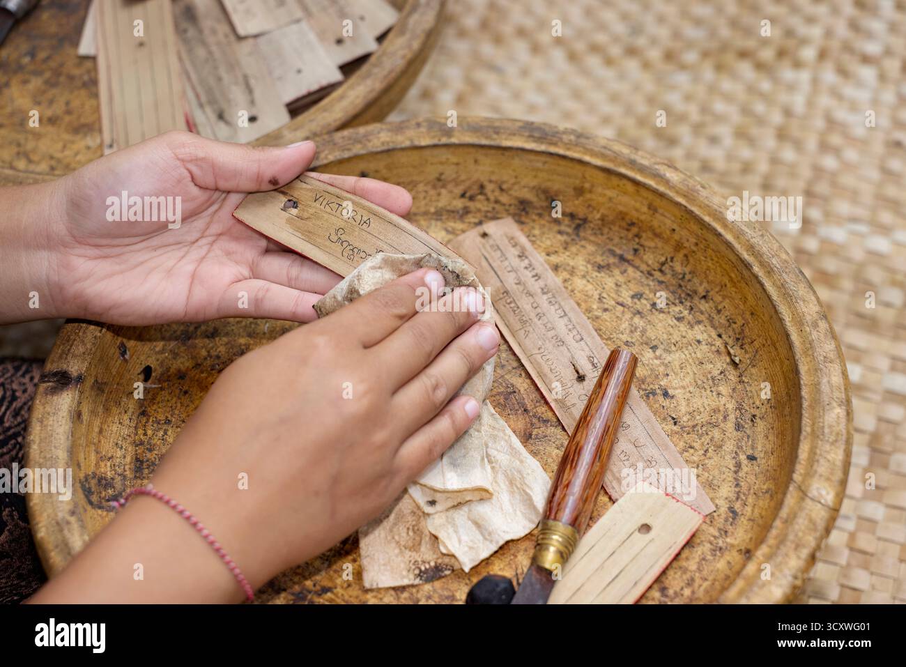 L'artigiana balinese realizza un lontar (manoscritto di foglie di palma essiccate) con il nome del cliente nella traslitterazione balinese. Karangasem, Bali, Indonesia. Foto Stock